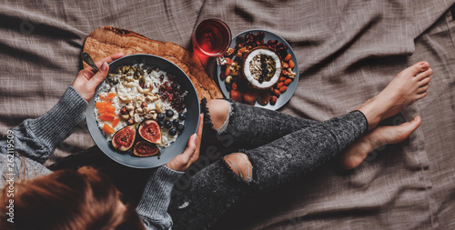 Woman in woolen sweater and jeans eating vegan Rice coconut porridge with figs, berries, nuts. Healthy breakfast ingredients. Clean eating, vegan food concept