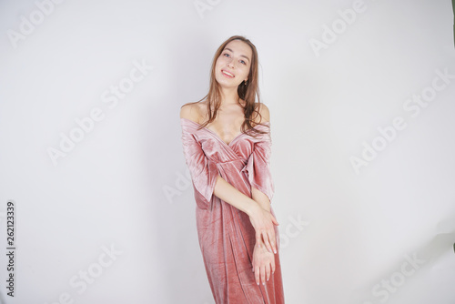 cute young caucasian teenager girl in pink velvet dress stands and smiles on white background in Studio