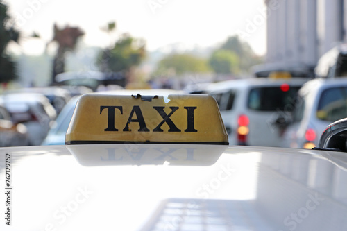 Broken taxi light sign or cab sign in drab yellow color with black text on the car roof at the street blurred background.