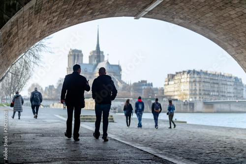 Tourists strolling on the banks of Seine under the bridge Alexandre III with the Notre Dame cathedral in the background