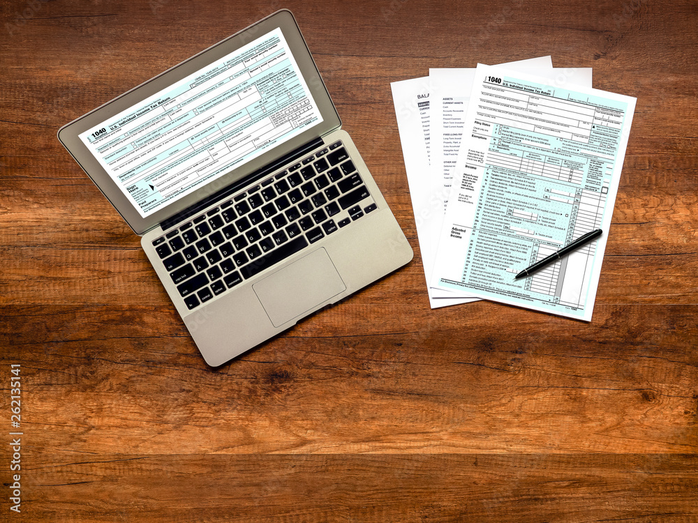 Obraz premium U.S. Individual income tax return on wooden table. Individual income tax return form online on laptop screen.