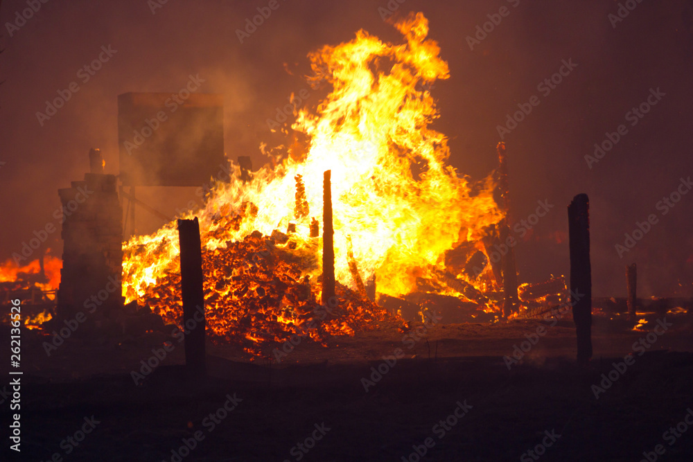 The fire wriggles over the burnt down building. A pile of flaming red coals on the site of a burnt house. Fire and smoke in a residential area at night. Burnt house.