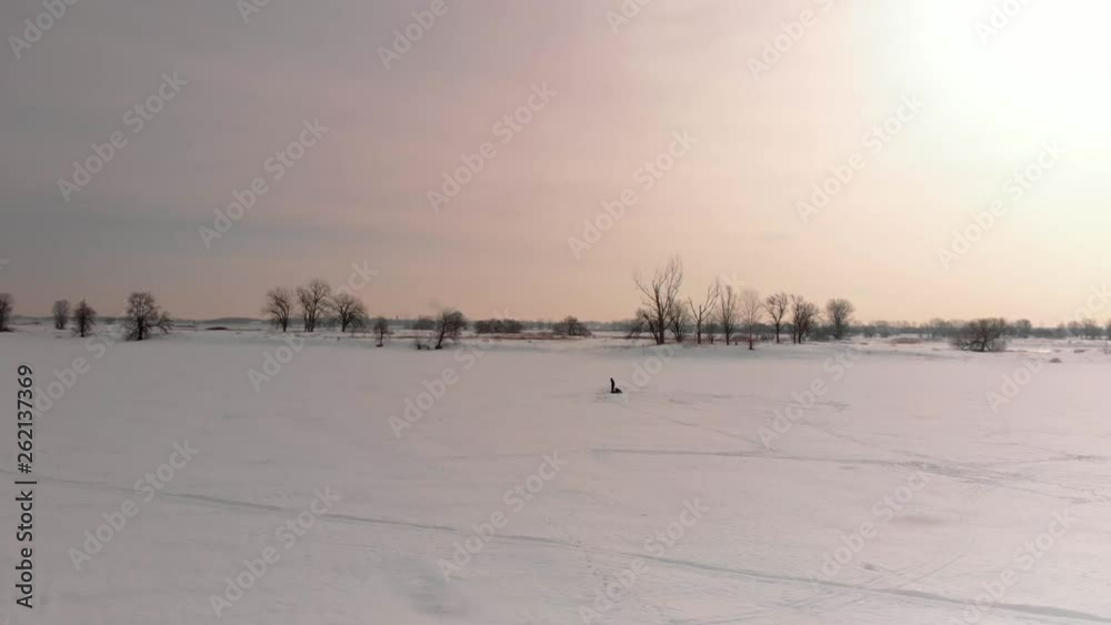 low altitude aerial shoot of frozen lake at sunset with shadow of a man fishing on ice low altitude aerial shoot of frozen lake at sunset with shadow of a man fishing on ice