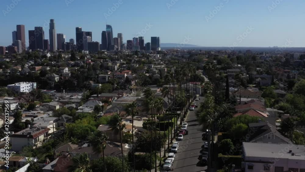 Drone flys over iconic Los Angeles palm tree lined street with the city skyline in the background. Drone flys over iconic Los Angeles palm tree lined street with the city skyline in the background.