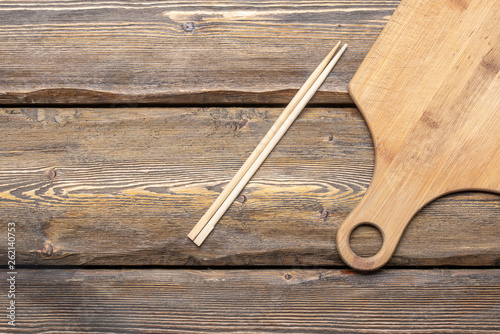 empty cutting board with chopsticks on wooden background, top view 