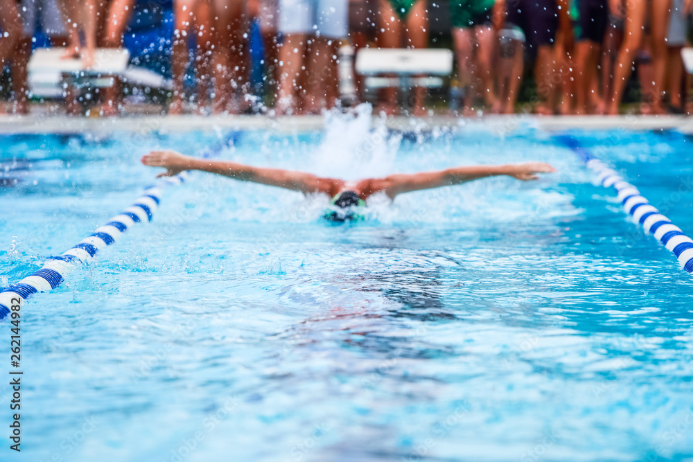 Man swimming butterfly stroke in a race, focus on waves, swimmer is out of focus