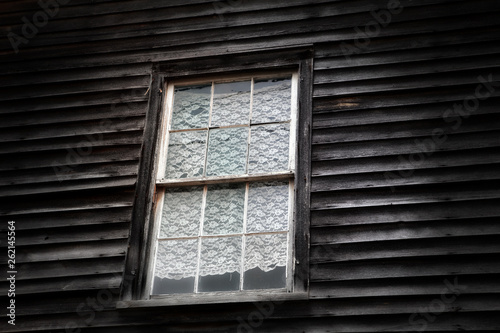 A lace curtain in a window in an old unpainted clapboard house