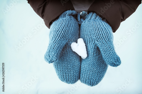 Heart shaped snow in blue knit mittens in the wintertime on a snowy day, blue tone