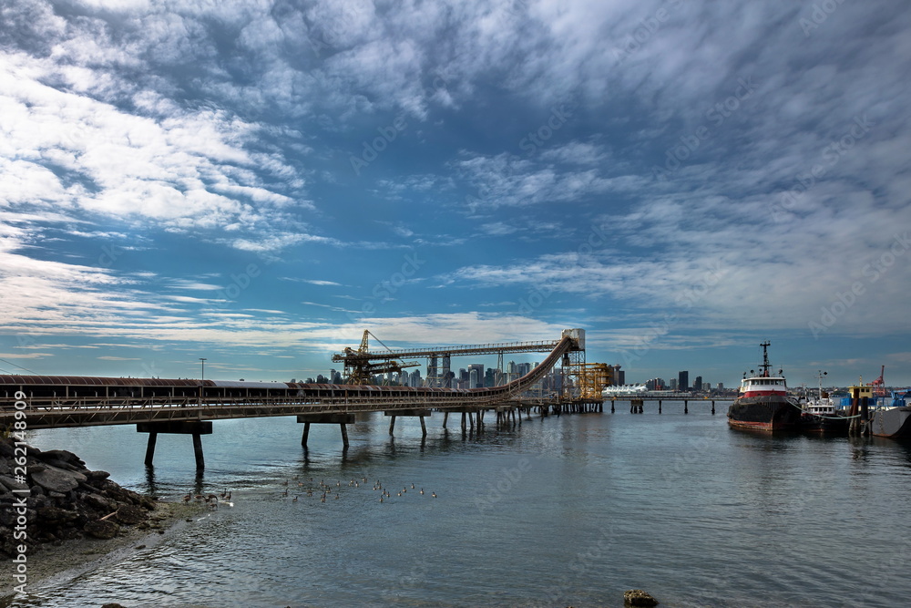 Loading conveyor at the cargo terminal of the port in North Vancouver, the blue sea and a beautiful cloudy sky against the background of  Vancouver downtown
