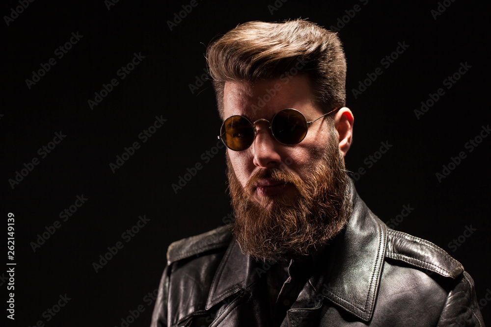 Elegant bearded man with leather jacket and sunglasses over black background Elegant bearded man with leather jacket and sunglasses over black background