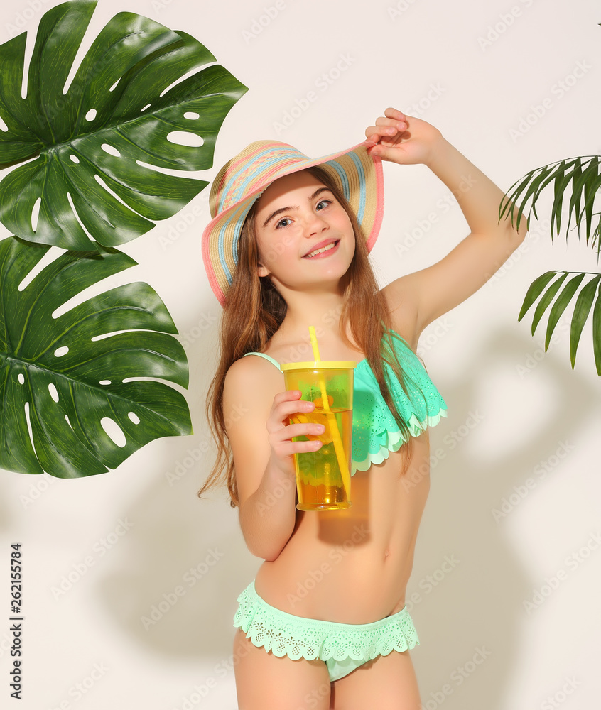 Charming 10 year old girl in swimsuit and hat with lemonade among tropical  green leaves on white background Photos | Adobe Stock