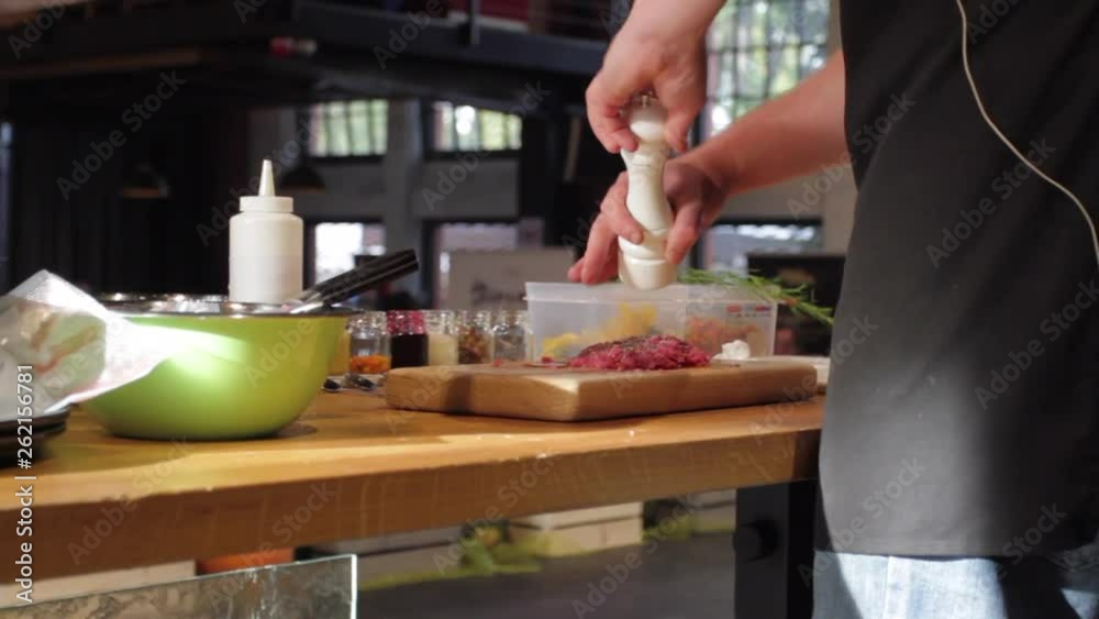 Chef is salting meat in front of the audience. Preparing minced meat for cooking. Closeup of master chef putting spices on fresh slice of meat. Chef is salting meat in front of the audience. Preparing minced meat for cooking. Closeup of master chef putting spices on fresh slice of meat.