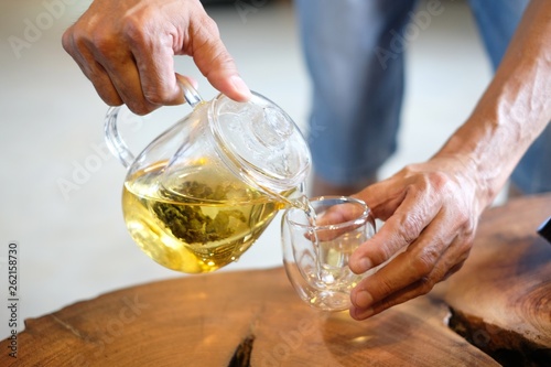 Hand that pours chinese green tea from glass kettle to small cup.