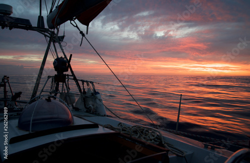 sailing during a magnificent orange, pink, and yellow sunset reflected on calm water