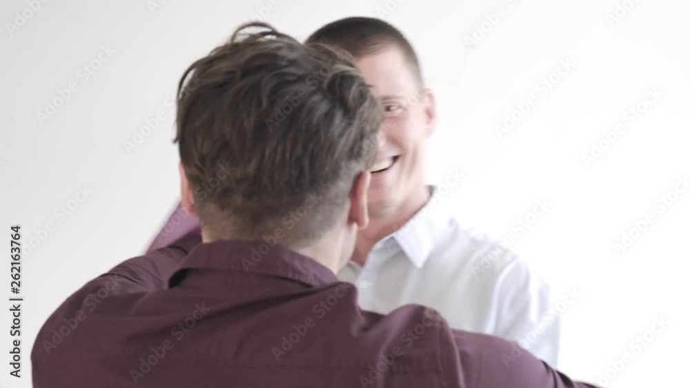 Young gay male couple holding pride flag in bedroom. Dancing happily.