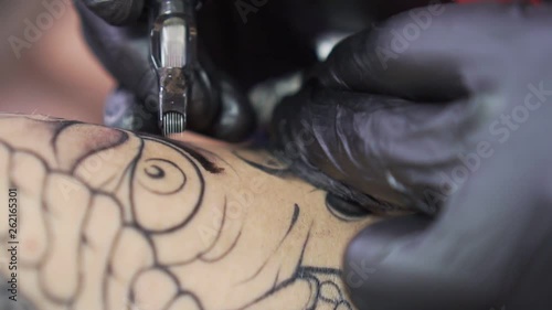 process of tattooing close-up. The needle of the tattoo machine inserts ink under the skin.