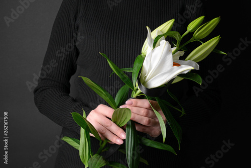 Mourning woman with lily flowers and black ribbon on dark background