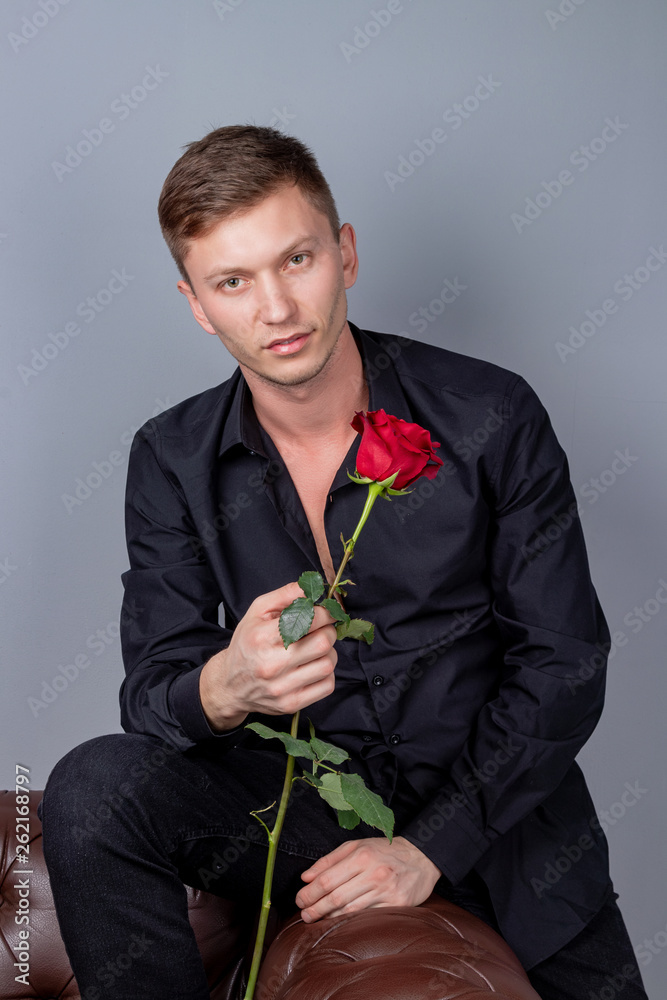 Handsome man wearing black shirt sitting on the leather sofa holding a rose and getting ready romantic date Handsome man wearing black shirt sitting on the leather sofa holding a rose and getting ready romantic date
