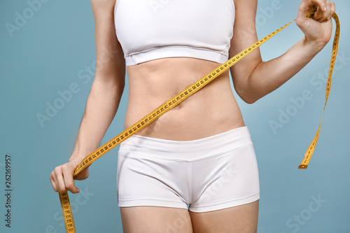 Sporty woman with measuring tape on color background