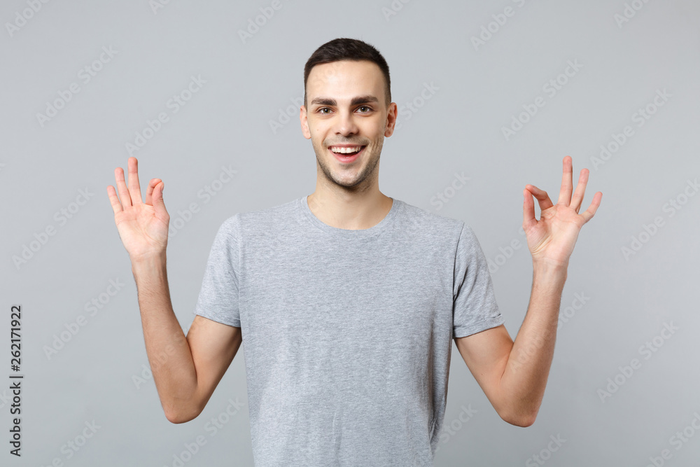 Fototapeta premium Portrait of smiling young man in casual clothes holding hands in yoga gesture relaxing meditating isolated on grey background in studio. People sincere emotions, lifestyle concept. Mock up copy space.