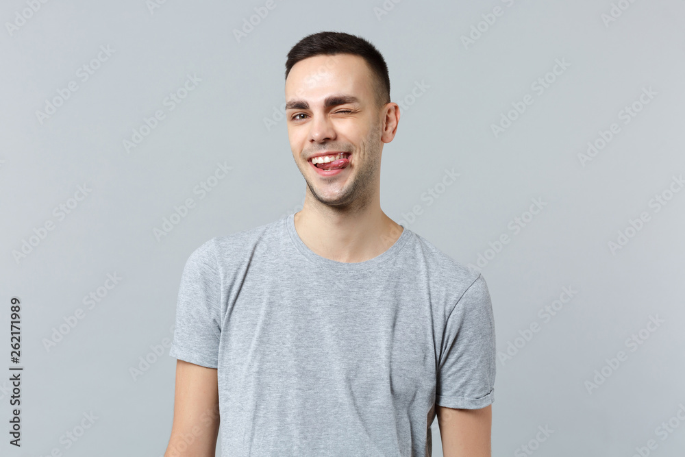 Portrait of cheerful funny blinking young man in casual clothes looking camera showing tongue isolated on grey wall background in studio. People sincere emotions lifestyle concept. Mock up copy space. Portrait of cheerful funny blinking young man in casual clothes looking camera showing tongue isolated on grey wall background in studio. People sincere emotions lifestyle concept. Mock up copy space.