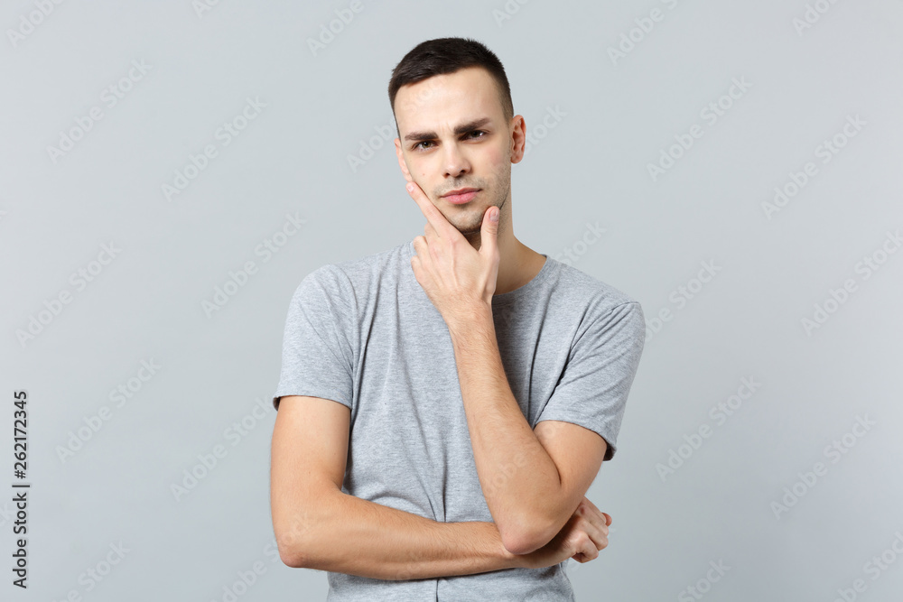 Portrait of pensive puzzled young man in casual clothes looking camera put hand prop up on chin isolated on grey background in studio. People sincere emotions lifestyle concept. Mock up copy space. Portrait of pensive puzzled young man in casual clothes looking camera put hand prop up on chin isolated on grey background in studio. People sincere emotions lifestyle concept. Mock up copy space.