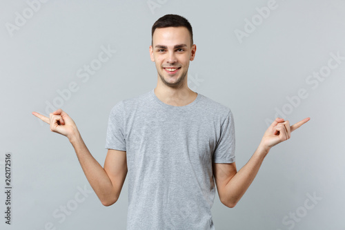 Portrait of handsome young man in casual clothes looking camera pointing index fingers aside isolated on grey wall background in studio. People sincere emotions, lifestyle concept. Mock up copy space.