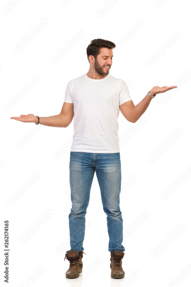 Young Man In Jeans And White T-shirt Is Standing And Compare Something. Young Man In Jeans And White T-shirt Is Standing And Compare Something.