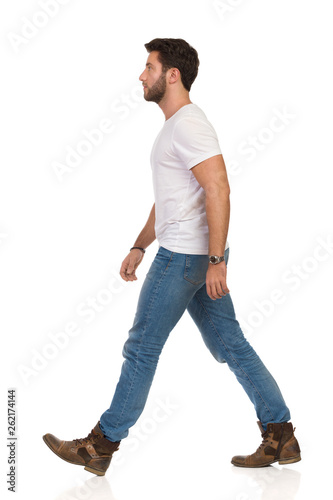 Serious Young Man In Jeans And White T-shirt Is Walking. Side View