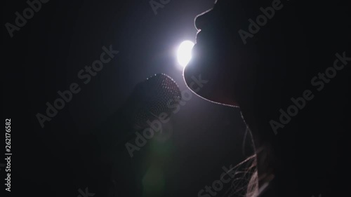 Close-up of the face of the singer with microphone on a black smoky background. The singer sings a song on stage in the dark, smoke, purple light, concert 4k