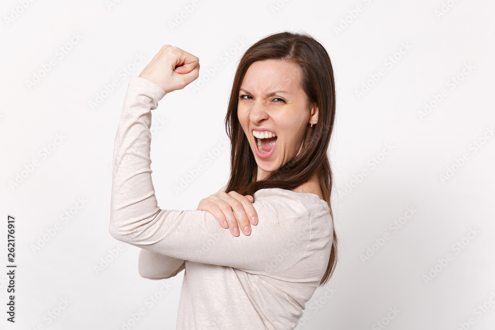 Portrait of strong crazy screaming young woman in light clothes showing biceps, muscles isolated on white wall background in studio. People sincere emotions, lifestyle concept. Mock up copy space. Portrait of strong crazy screaming young woman in light clothes showing biceps, muscles isolated on white wall background in studio. People sincere emotions, lifestyle concept. Mock up copy space.