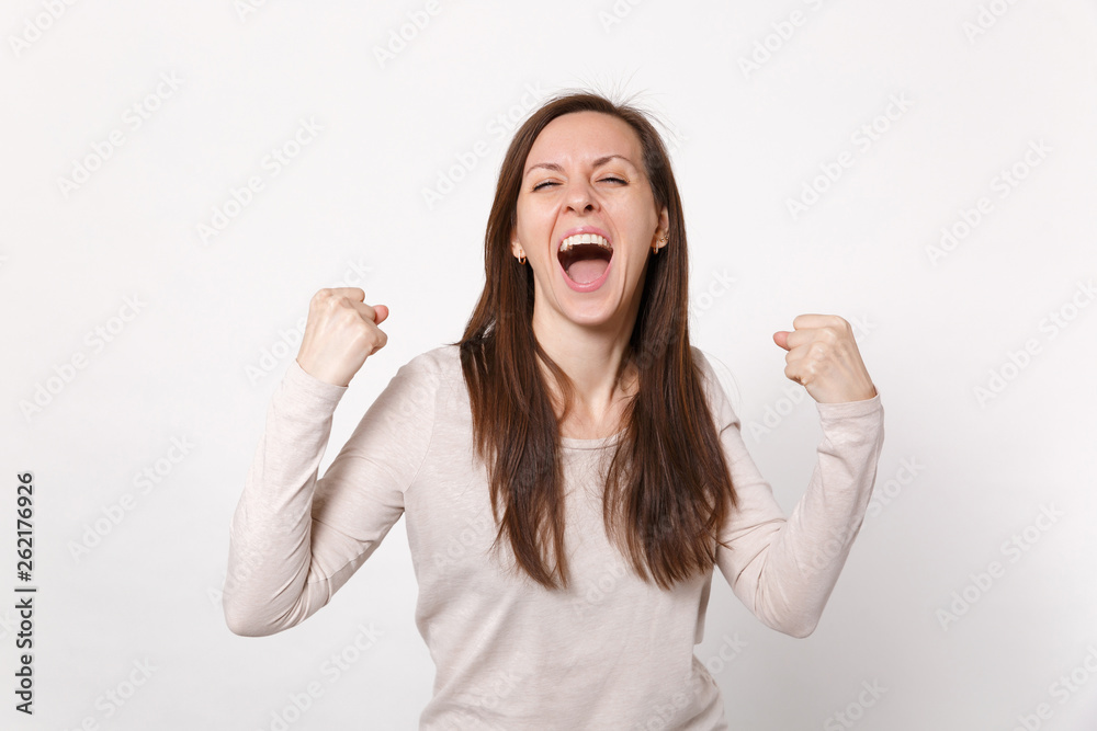 Portrait of overjoyed screaming young woman in light clothes keeping eyes closed doing winner gesture isolated on white wall background. People sincere emotions, lifestyle concept. Mock up copy space. Portrait of overjoyed screaming young woman in light clothes keeping eyes closed doing winner gesture isolated on white wall background. People sincere emotions, lifestyle concept. Mock up copy space.