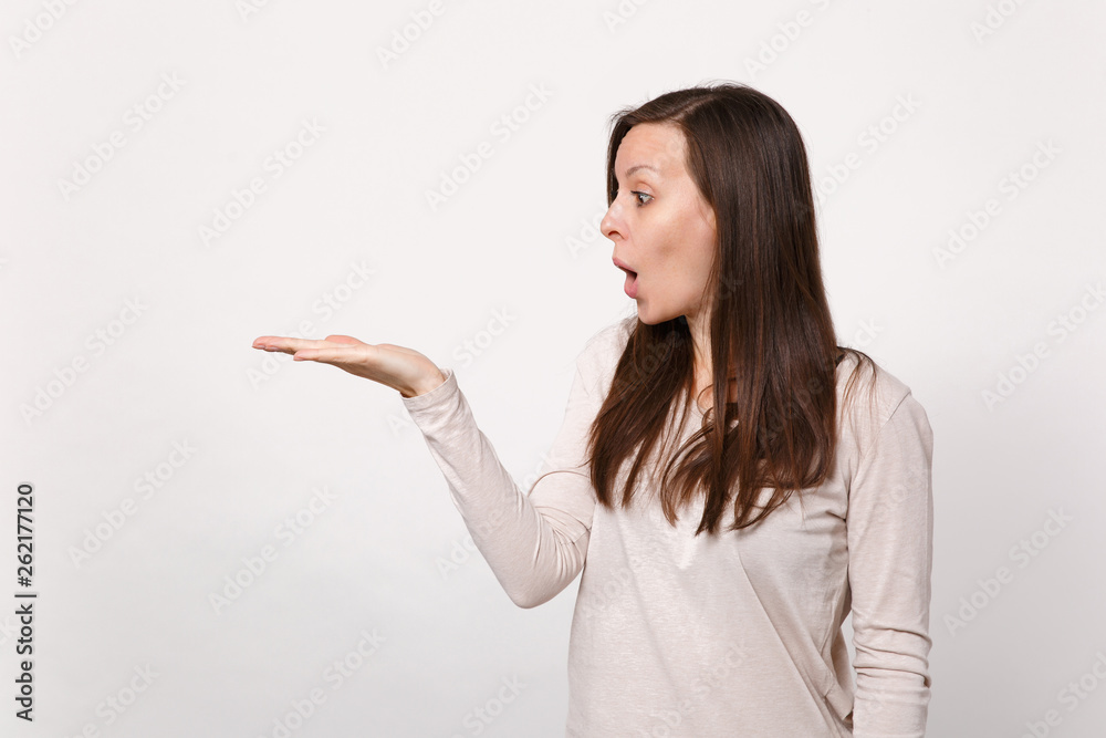 Portrait of shocked young woman in light clothes looking, pointing hand aside keeping mouth open isolated on white background in studio. People sincere emotions, lifestyle concept. Mock up copy space. Portrait of shocked young woman in light clothes looking, pointing hand aside keeping mouth open isolated on white background in studio. People sincere emotions, lifestyle concept. Mock up copy space.