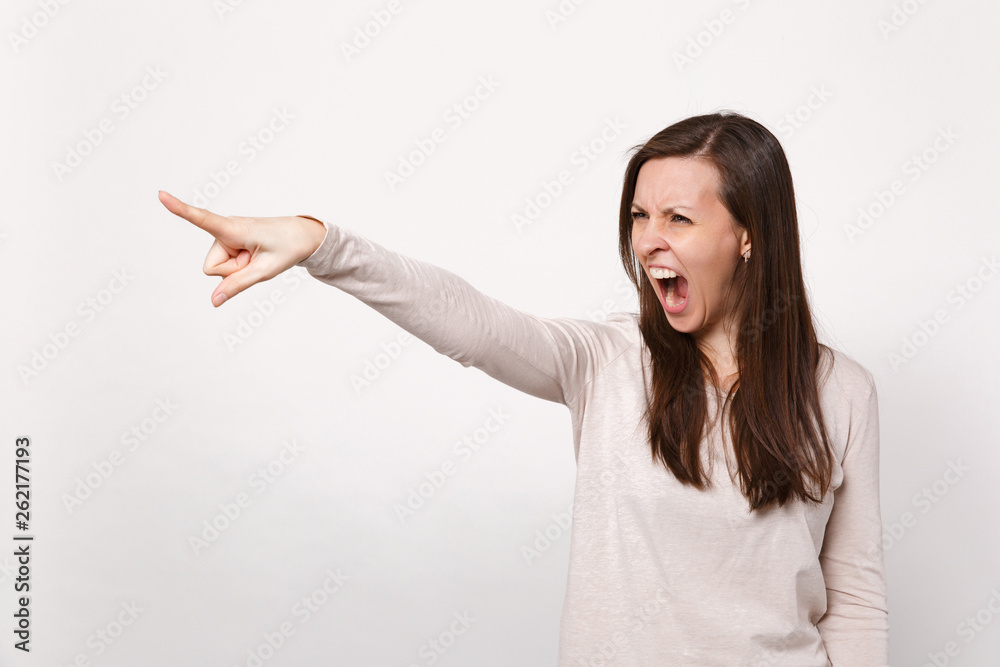 Portrait of irritated screaming young woman in light clothes swearing looking, pointing index finger aside isolated on white background. People sincere emotions, lifestyle concept. Mock up copy space. Portrait of irritated screaming young woman in light clothes swearing looking, pointing index finger aside isolated on white background. People sincere emotions, lifestyle concept. Mock up copy space.