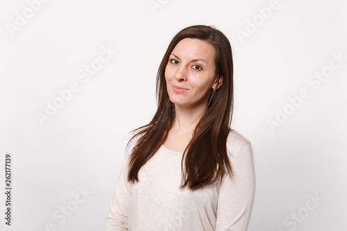 Portrait of smiling attractive young woman in light clothes standing and looking camera isolated on white wall background in studio. People sincere emotions lifestyle concept. Mock up copy space.