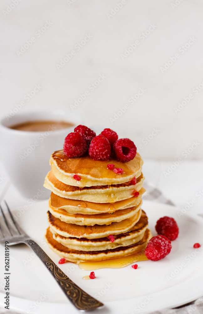 Tall stack of pancakes with honey and raspberries on white plate. Breakfast for the whole family 