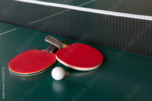Two ping-pong rackets and a ball on a green table. Close-up