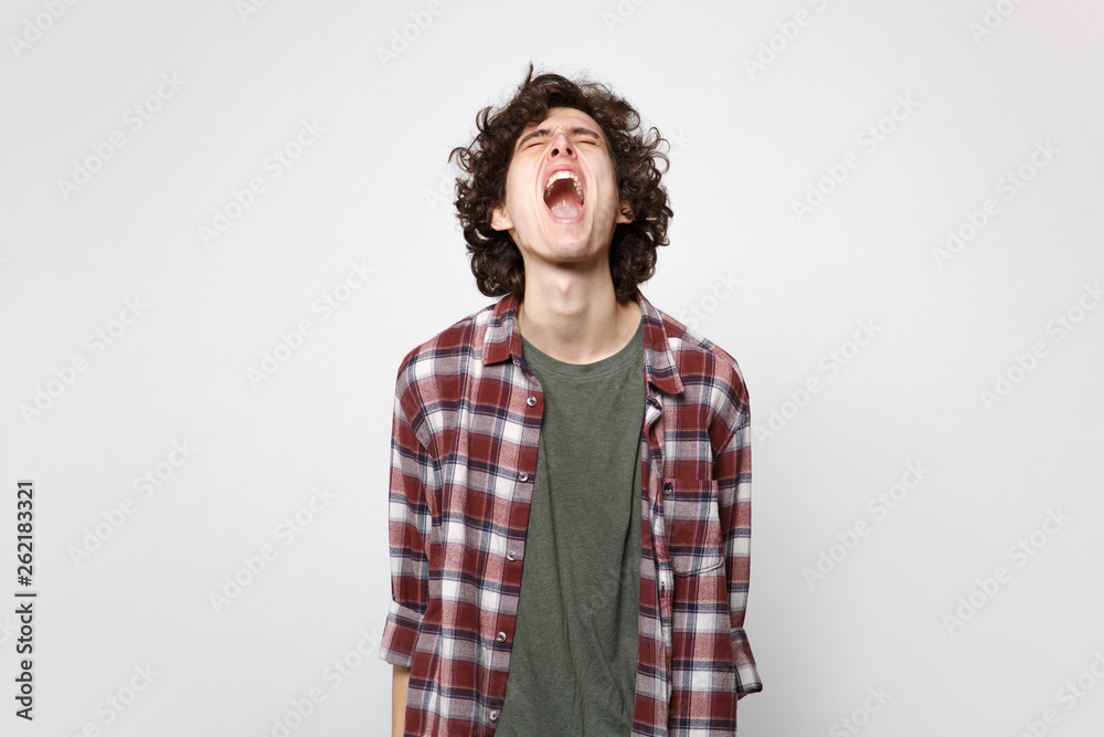 Portrait of crazy wild screaming young man in casual clothes standing, keeping eyes closed isolated on white wall background in studio. People sincere emotions, lifestyle concept. Mock up copy space. Portrait of crazy wild screaming young man in casual clothes standing, keeping eyes closed isolated on white wall background in studio. People sincere emotions, lifestyle concept. Mock up copy space.