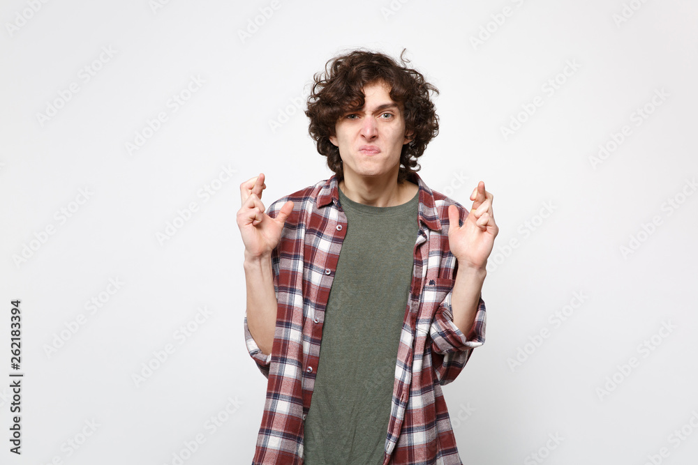 Displeased young man in casual clothes waiting for special moment, keeping fingers crossed making wish isolated on white wall background. People sincere emotions lifestyle concept. Mock up copy space. Displeased young man in casual clothes waiting for special moment, keeping fingers crossed making wish isolated on white wall background. People sincere emotions lifestyle concept. Mock up copy space.