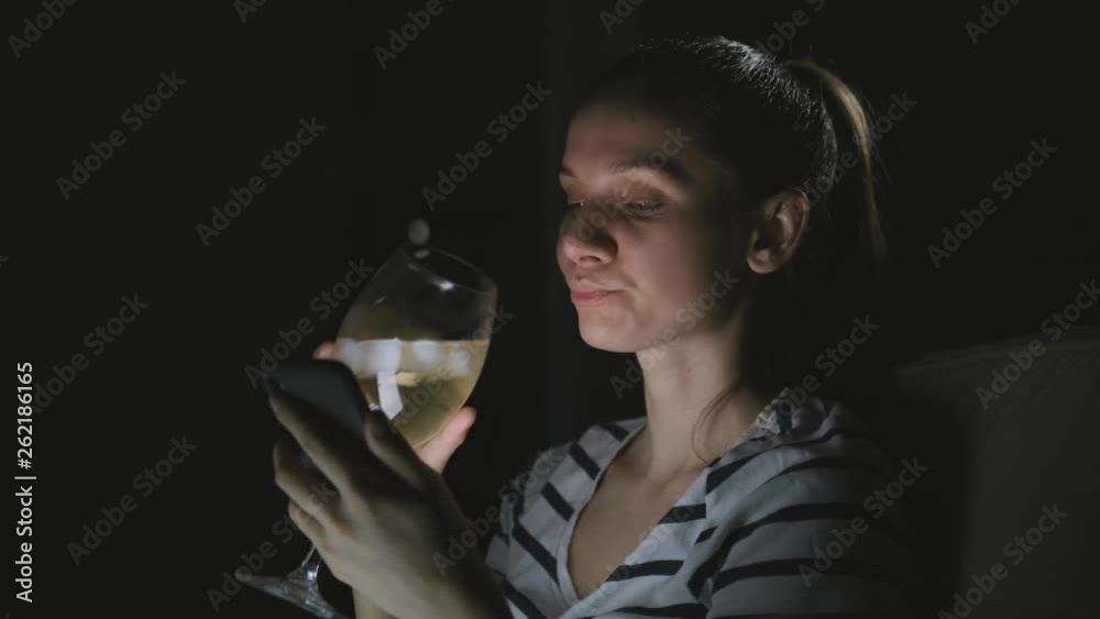 young brunette woman sitting on the sofa, drinking wine and talking on the phone in the evening young brunette woman sitting on the sofa, drinking wine and talking on the phone in the evening