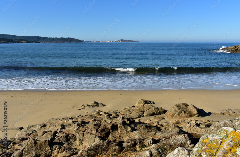 Beach with rocks, wet sand and waves with foam. Blue sky, sunny day, Galicia, Spain. Beach with rocks, wet sand and waves with foam. Blue sky, sunny day, Galicia, Spain.