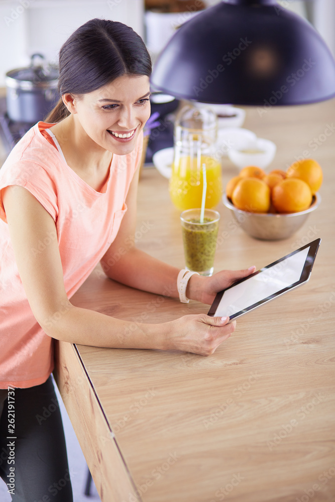 Beautiful young woman using a digital tablet in the kitchen