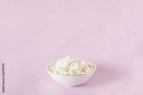 Fresh cottage cheese for breakfast in a white bowl in the center of the frame on a pink background