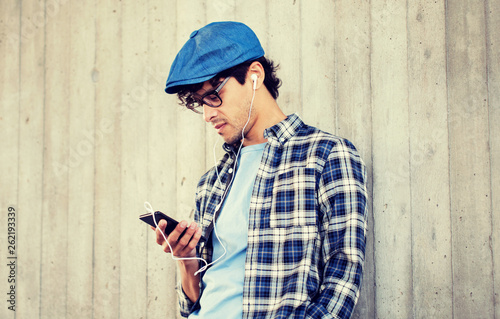 people, music, technology, leisure and lifestyle - young hipster man with earphones and smartphone listening to music