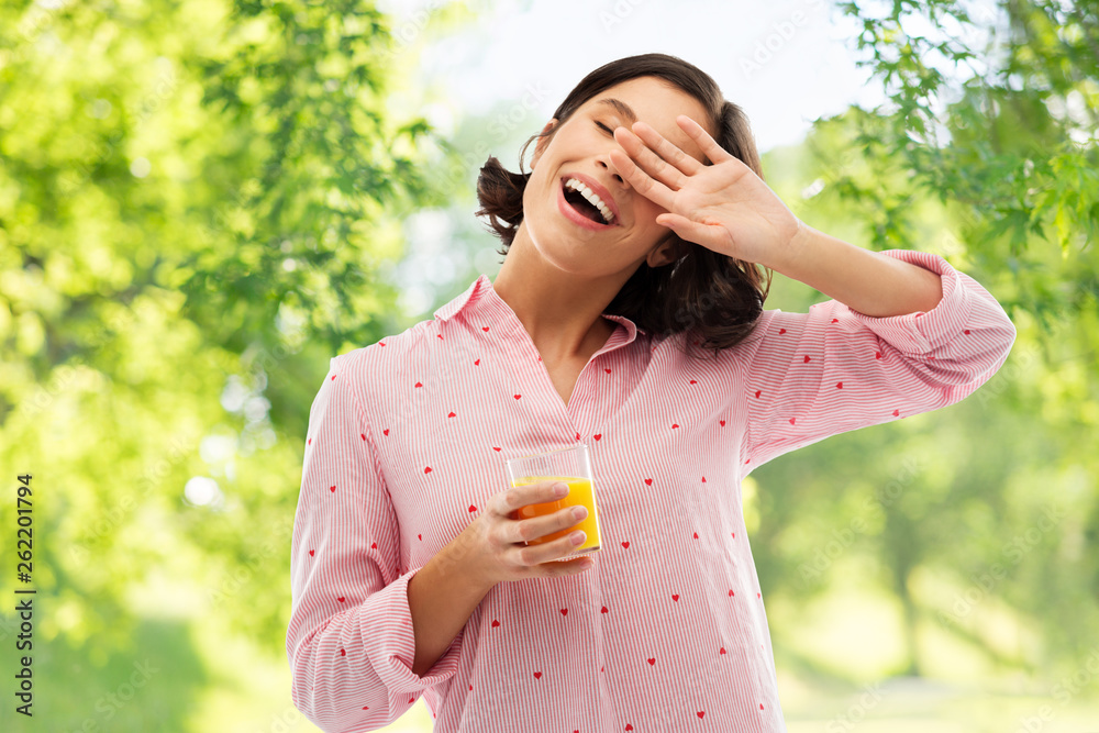 people and morning concept - happy yawning sleepy young woman in pajama with glass of orange juice over green natural background people and morning concept - happy yawning sleepy young woman in pajama with glass of orange juice over green natural background