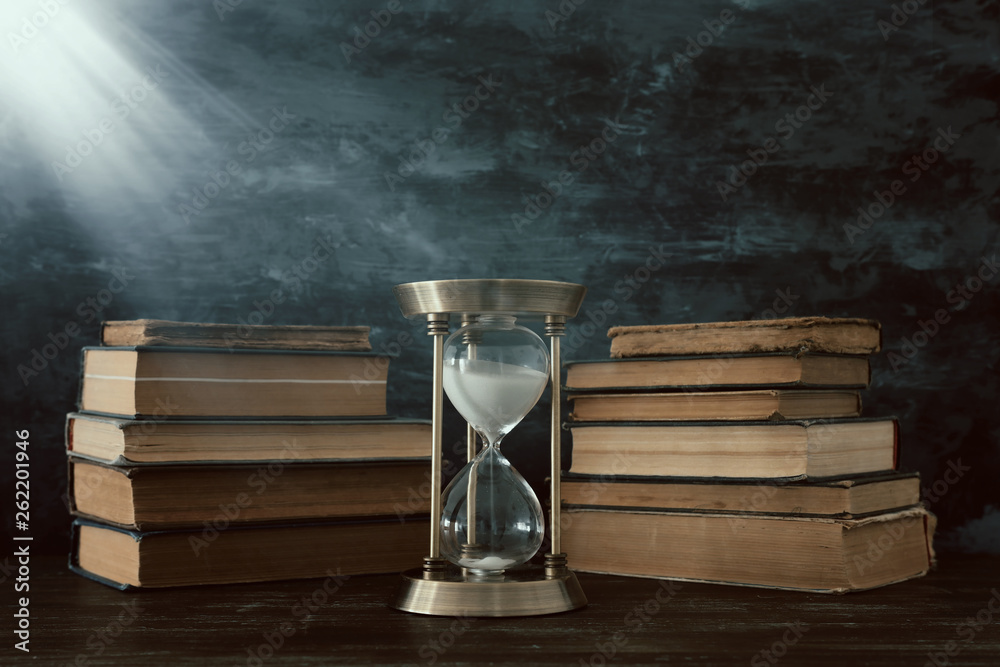 Hourglass as time passing concept and old books in front of black wall ...