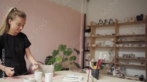 Tracking left medium shot of beautiful blonde ceramic artist cutting piece of clay off bar with string in her studio photo