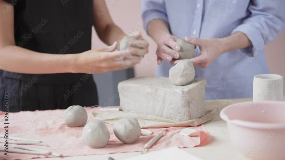 Сlose-up of young ceramic artist teaching adult female student how to wedge clay and form future bowl during personal class in art studio Сlose-up of young ceramic artist teaching adult female student how to wedge clay and form future bowl during personal class in art studio