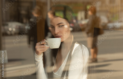 Girl holds a coffee cup at local coffee shop, concept photo through window for city effect with reflection
