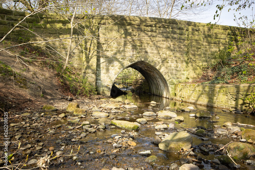 An old stone bridge with pointed arch carries a road over a small beck in Yorkshire photo